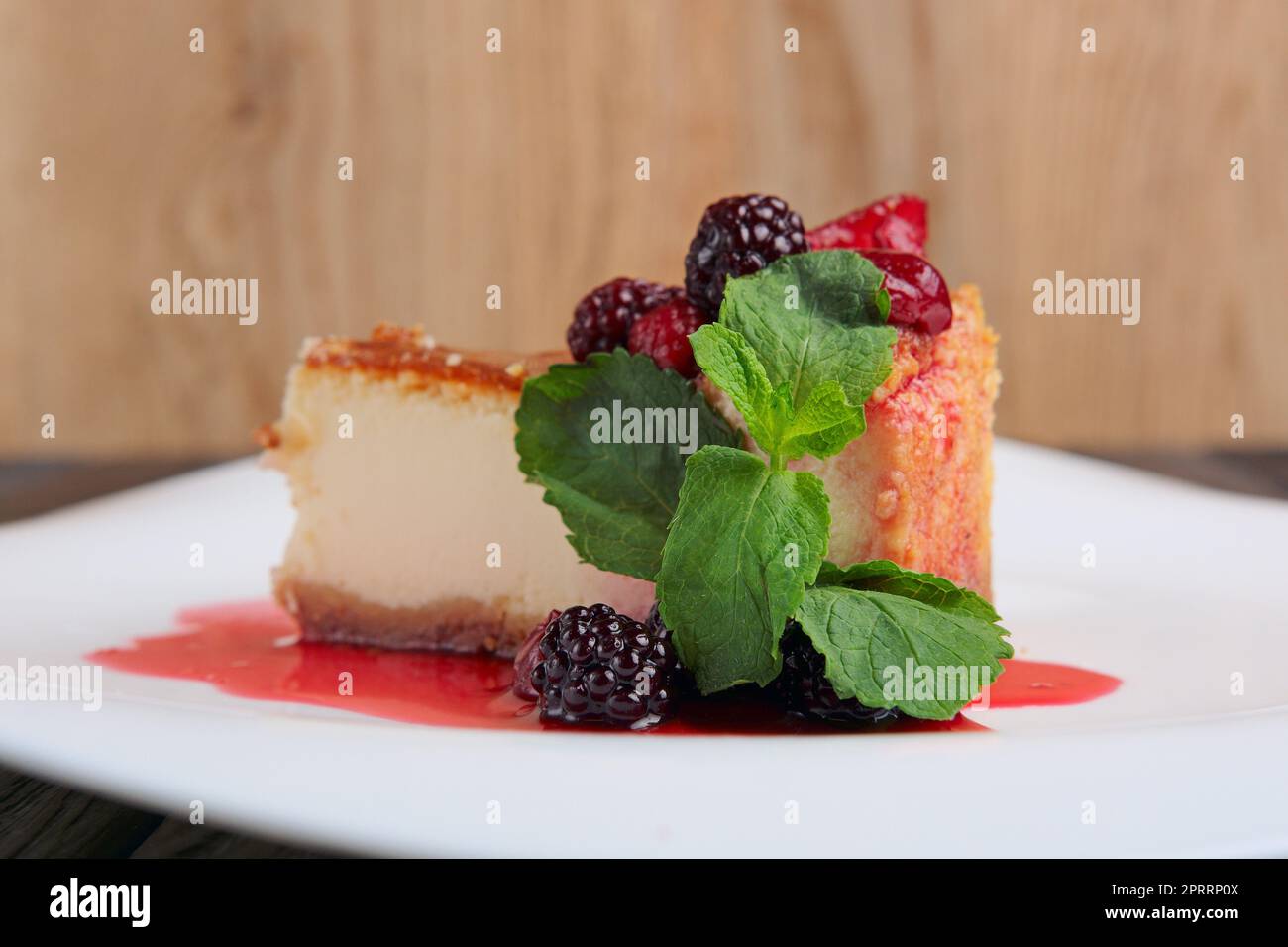 Pezzo di cheesecake con ciliegia, fragola e mirtillo decorato con sciroppo e foglie di menta sul tavolo Foto Stock