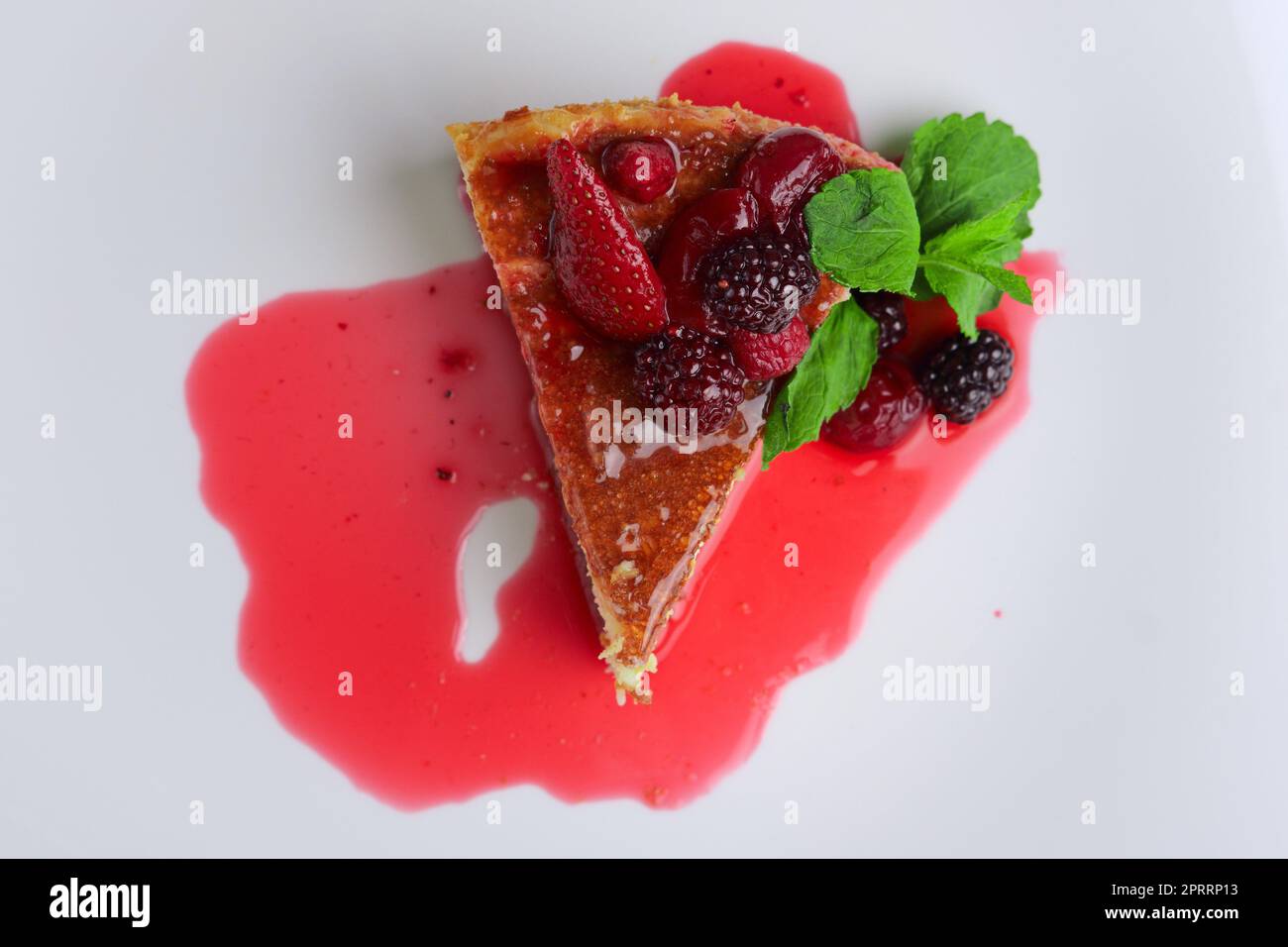 Vista dall'alto della cheesecake con ciliegia, fragola e mora decorata con sciroppo e foglie di menta Foto Stock
