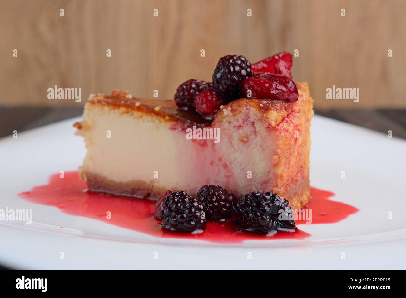 Fetta di cheesecake con ciliegia, fragola e mora decorata con sciroppo Foto Stock