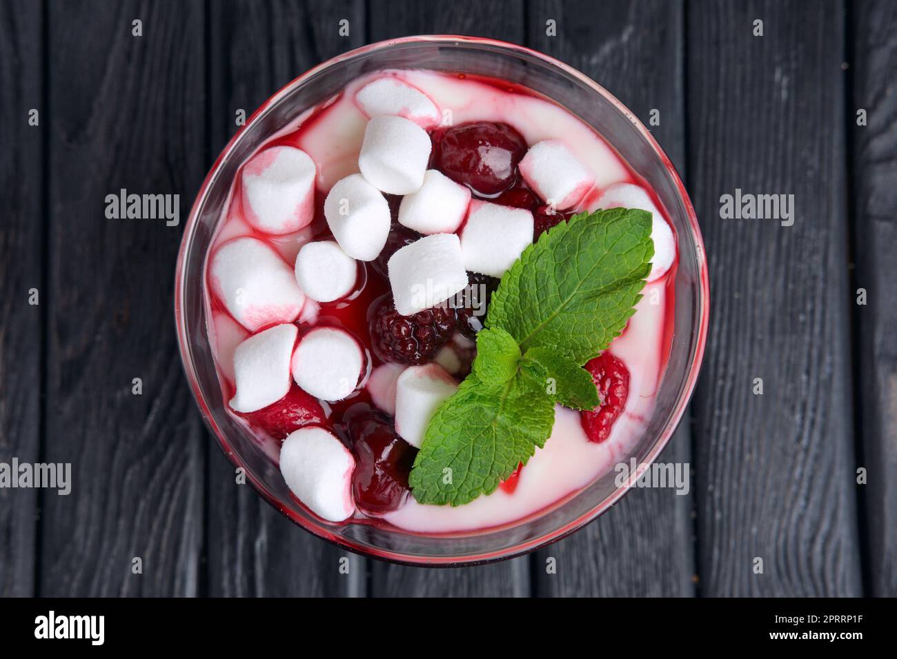 Un bicchiere di youghurt con marshmallow e lamponi decorato con foglie di menta. Vista dall'alto. Foto Stock