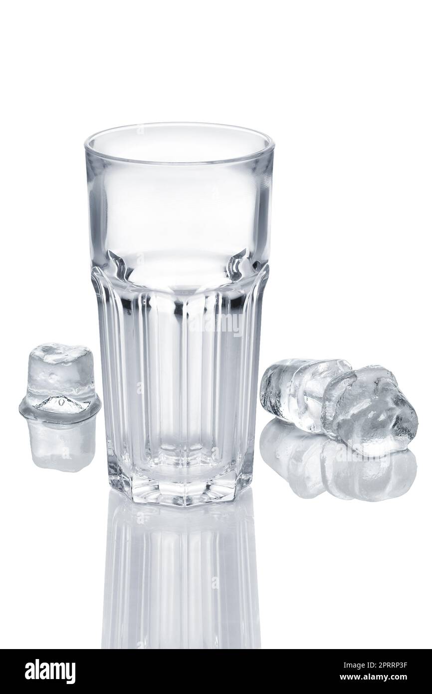 Vetro sfaccettato vuoto e tre cubetti di ghiaccio che si fondono su un tavolo di vetro bianco Foto Stock