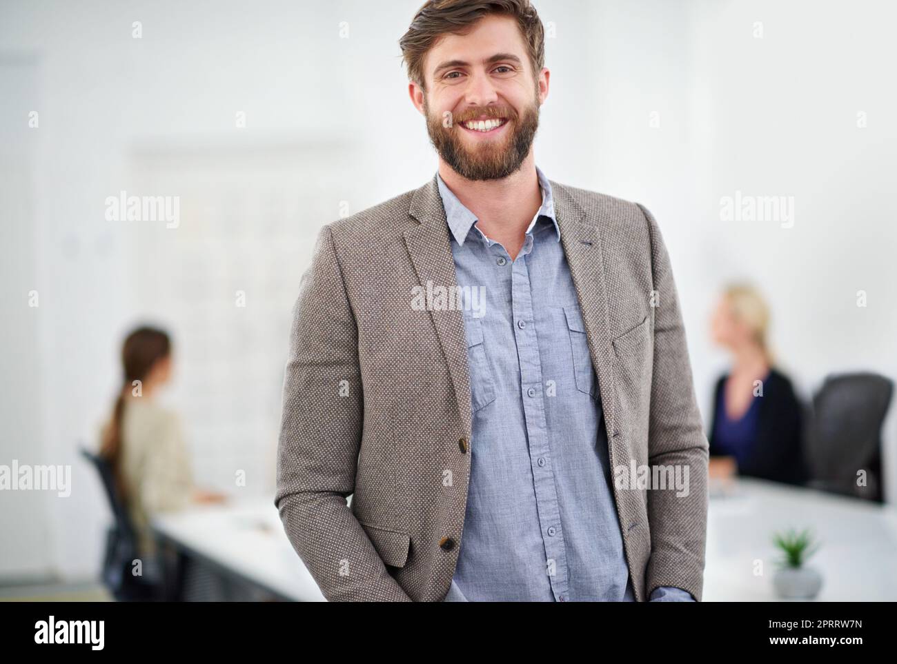 Sorridere è un modo per arrivare in cima. Ritratto di un giovane imprenditore in una sala conferenze con i colleghi sullo sfondo. Foto Stock