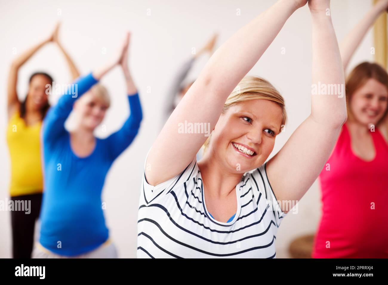 Yoga gioioso. Un gruppo multietnico di donne incinte che fanno esercizi con le braccia tese verso l'alto. Foto Stock