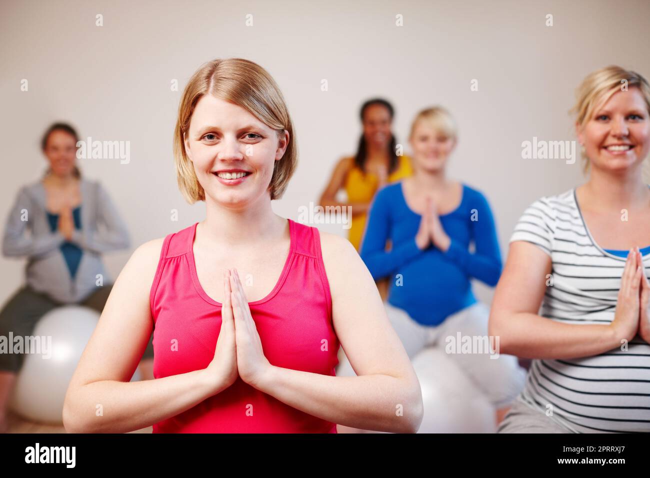 Meditare sulla nostra maternità. Un gruppo multietnico di donne incinte che meditano sulle palle da ginnastica in una classe di yoga. Foto Stock