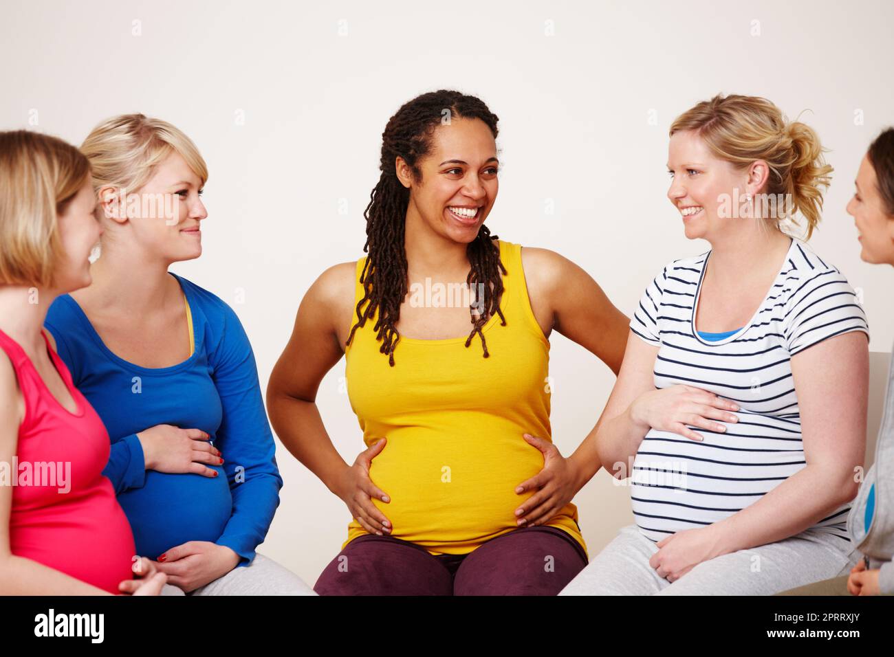 Sostentarsi l'un l'altro durante le loro gravidanze. Un gruppo multietnico di donne incinte sorridenti mentre si siedono insieme in cerchio. Foto Stock