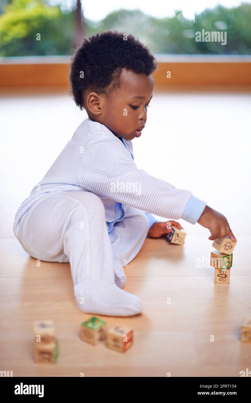 Rendalo divertente e l'apprendimento verrà. Un bambino cute che gioca con i blocchi di legno della costruzione sul pavimento. Foto Stock