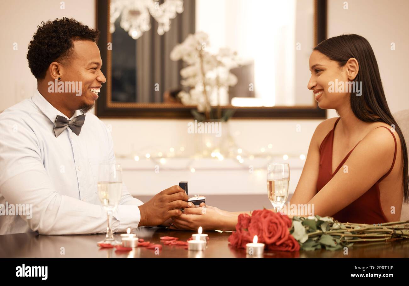 Fidanzamento, anello di proposta e coppia al ristorante con rose, regalo e festa d'amore. Gioielleria in giovani mani nere, donne o persone insieme a un tavolo di lusso con candele e bouquet Foto Stock