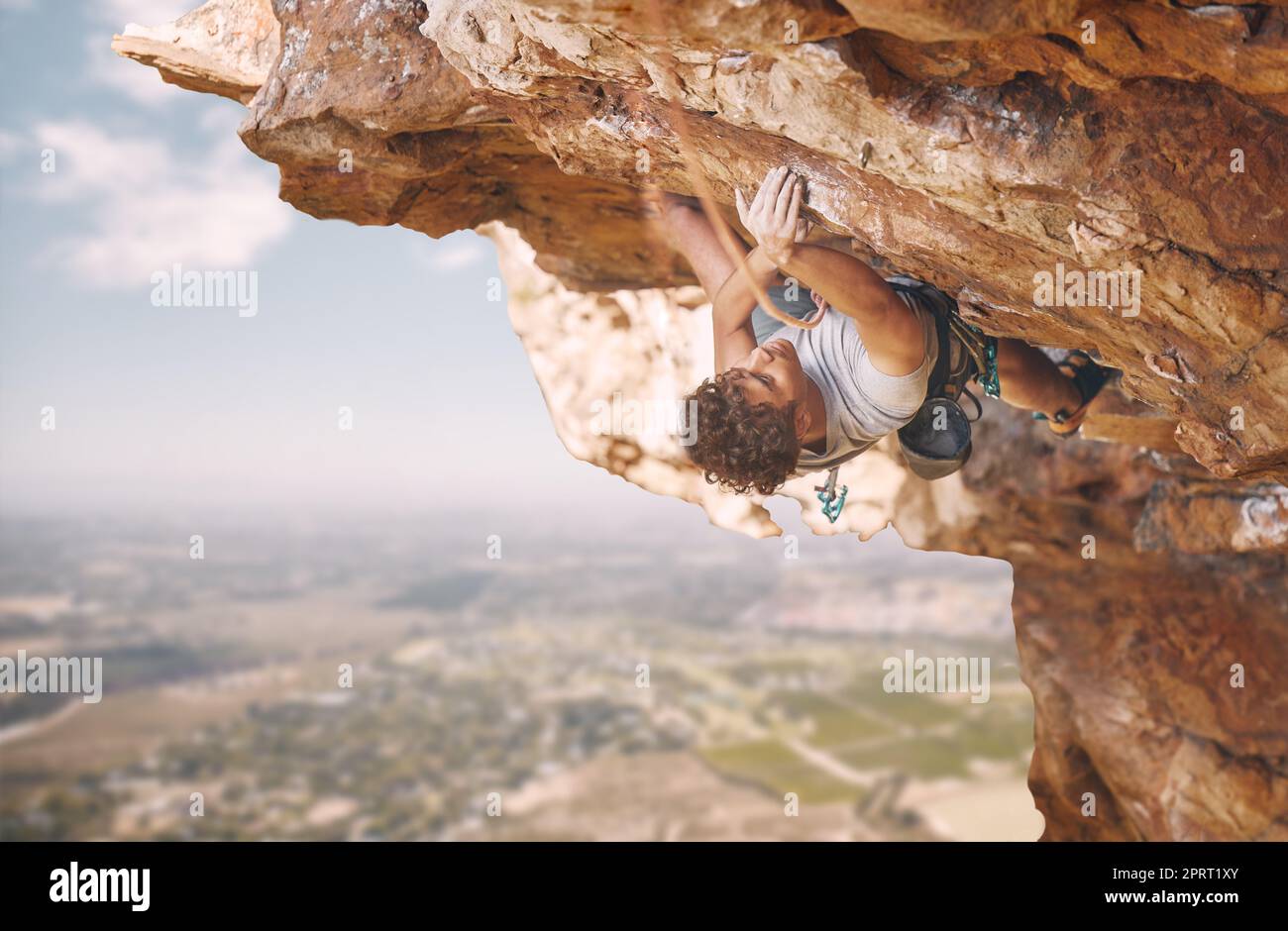 Sport di arrampicata su roccia e uomo sulla scogliera di montagna per il fitness all'aperto, l'obiettivo del benessere o la motivazione di allenamento. Avventura, energia sana di forte atleta bouldering in attrezzatura di sicurezza, corda sulla natura blu del cielo Foto Stock