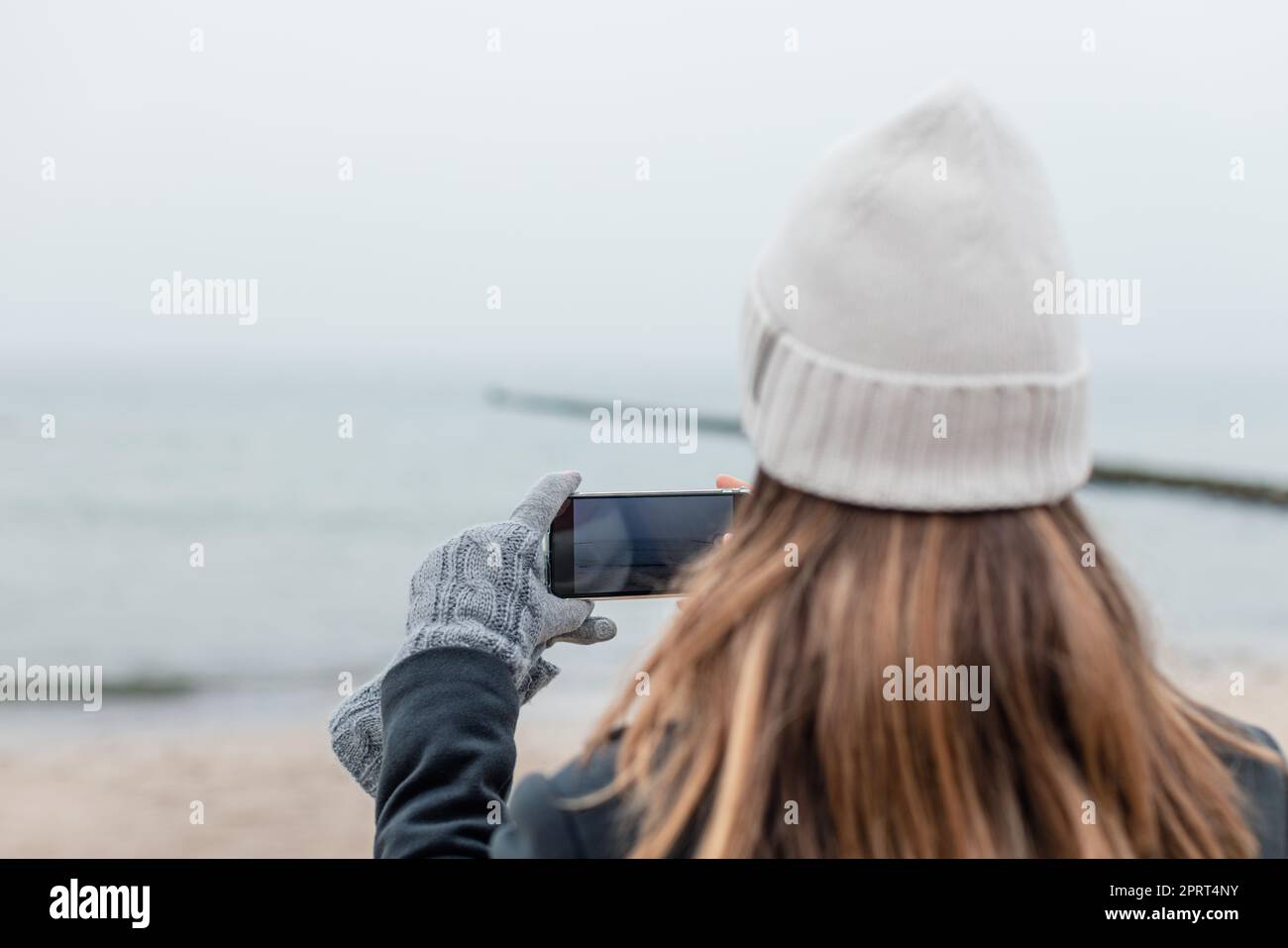 Donna che fotografa in spiaggia in inverno con il telefono Foto Stock