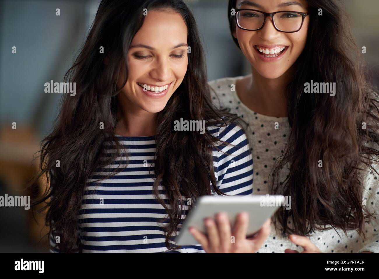 Sentirsi grandi per il mio lavoro e le relazioni. Bella giovane donna sorridente alla fotocamera mentre la sua amica guarda un tablet digitale. Foto Stock