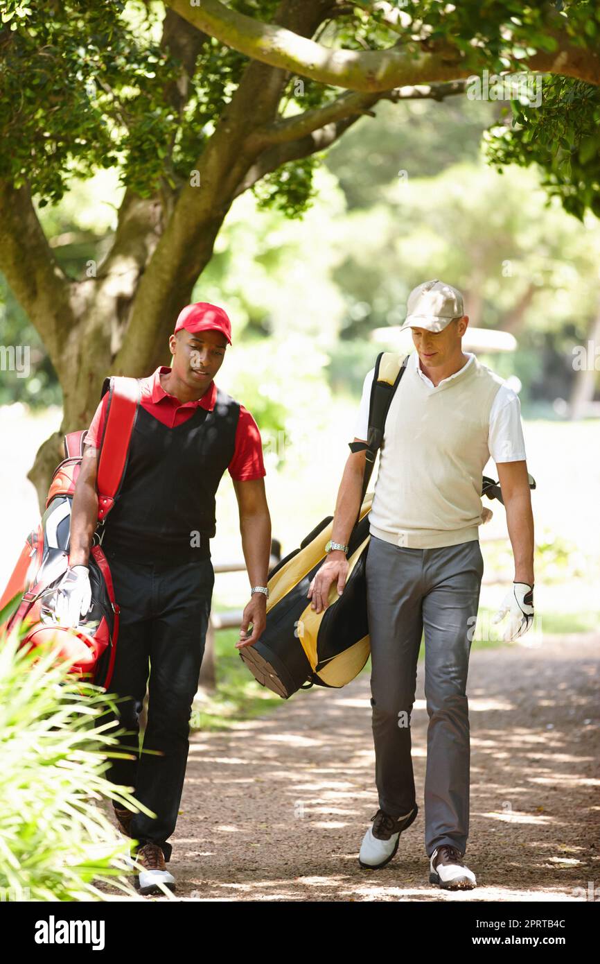 Tornando a casa dopo una giornata di golf, due uomini camminano lungo un sentiero ombreggiato su un campo da golf. Foto Stock