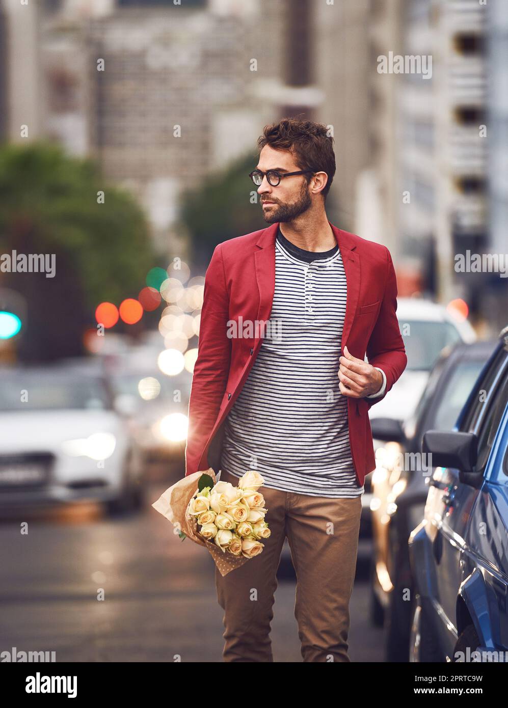 Fermare il traffico con il vostro fascino e gli sguardi. Un bel giovane che cammina sulla strada con le auto dietro di lui con un mazzo di fiori. Foto Stock