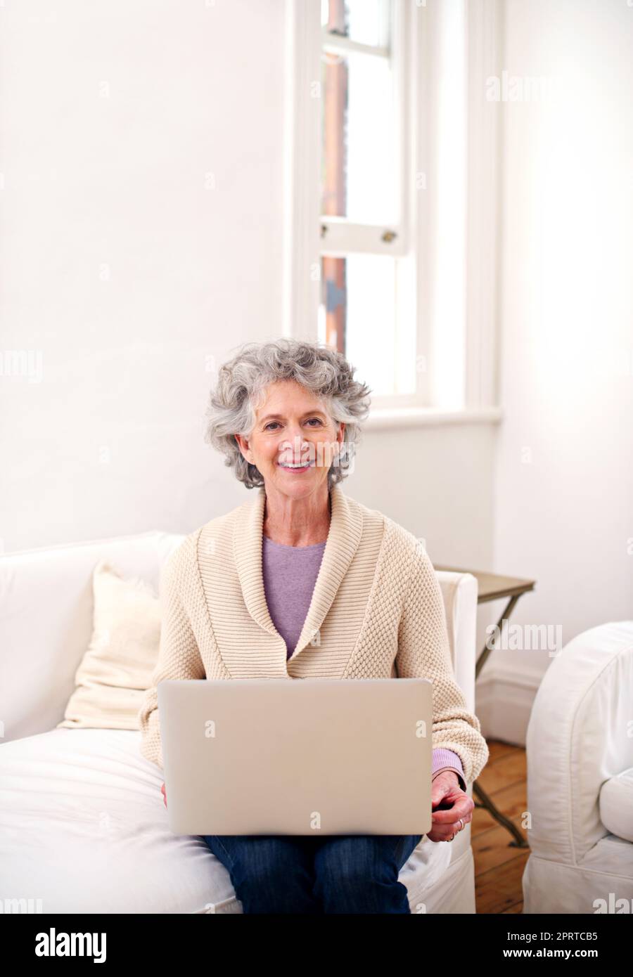 In contatto con i suoi vecchi amici. Una donna anziana seduta con un notebook su un divano. Foto Stock