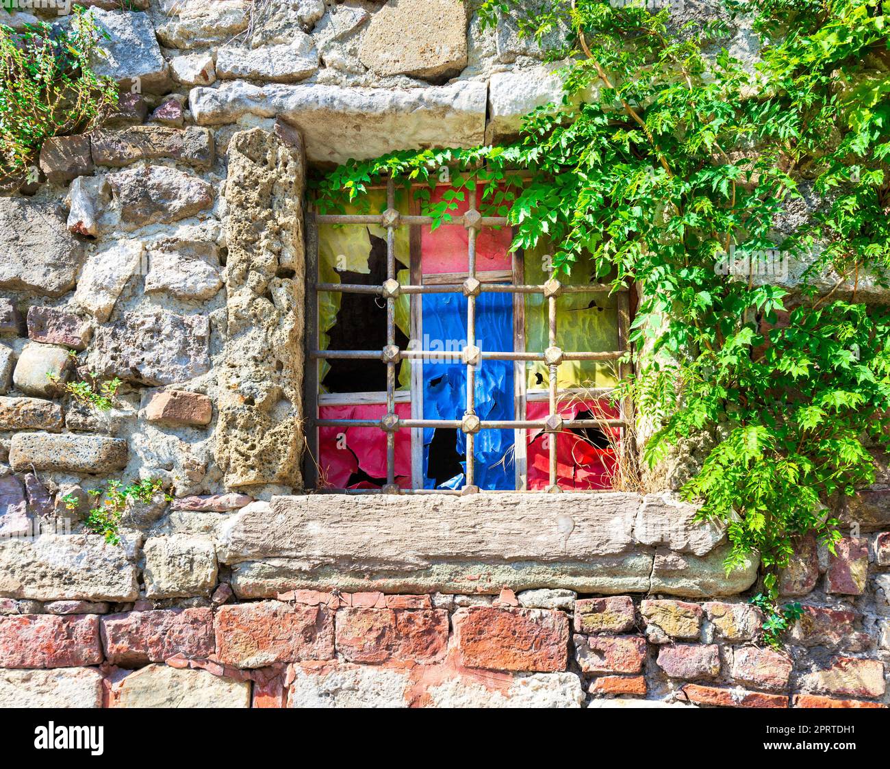 Vecchio muro di mattoni in pietra con finestra in ferro battuto grunge corroso e antico con quadrati colorati in più vivaci Foto Stock