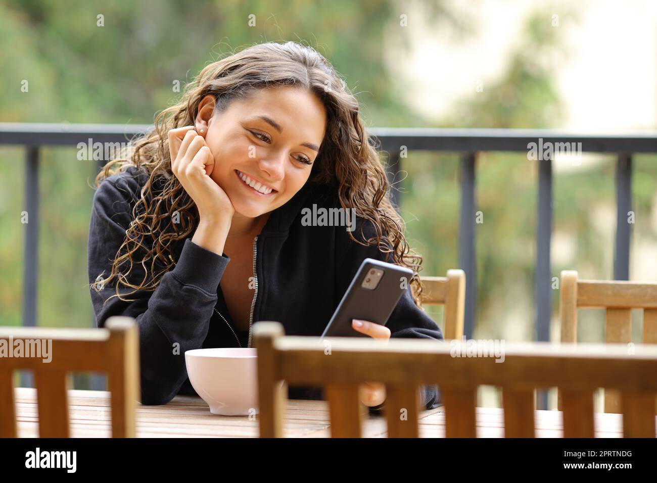 Donna in un balcone che sorride usando il telefono Foto Stock