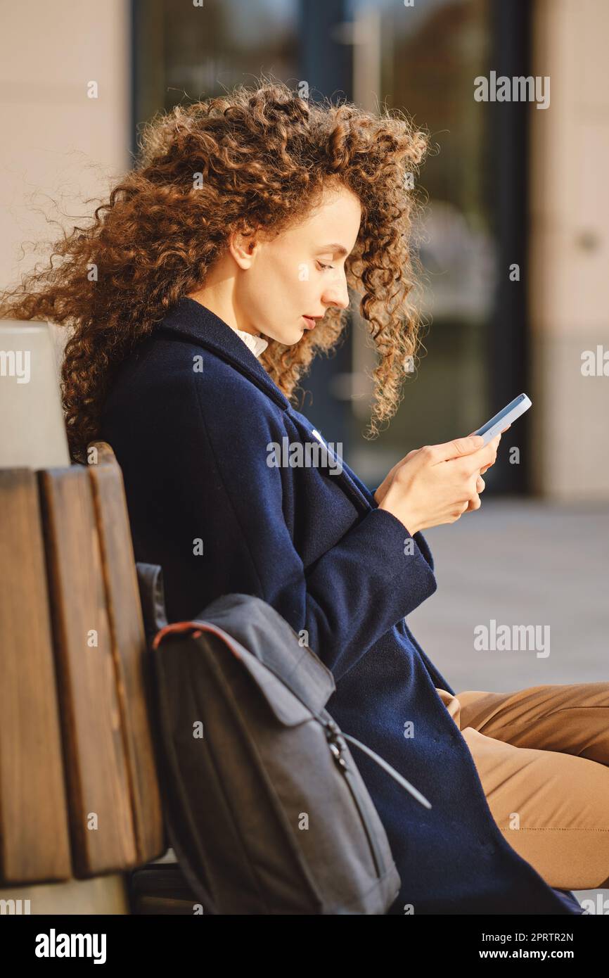 Giovane donna siede sulla panchina e cerca un appartamento in affitto nella città moderna Foto Stock