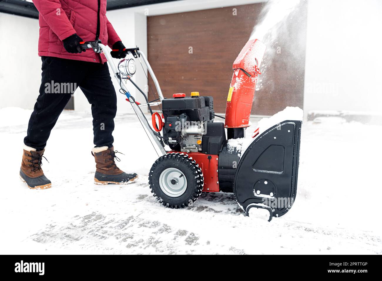 Uomo che usa una motoslitta rossa all'aperto. Rimozione della neve vicino alla casa dal cortile Foto Stock