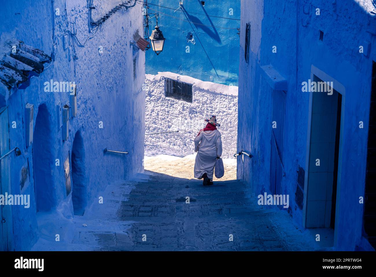 Donna che scende le scale di un vicolo ripido nella medina di Chefchaouen. Foto Stock