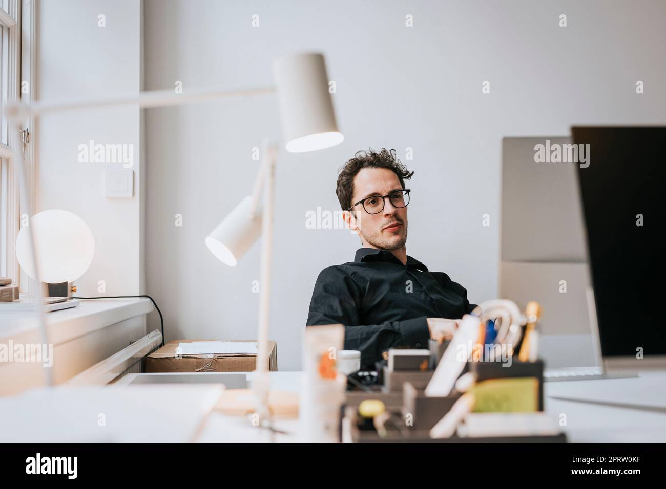 Uomo d'affari che indossa occhiali seduti alla scrivania in ufficio Foto Stock