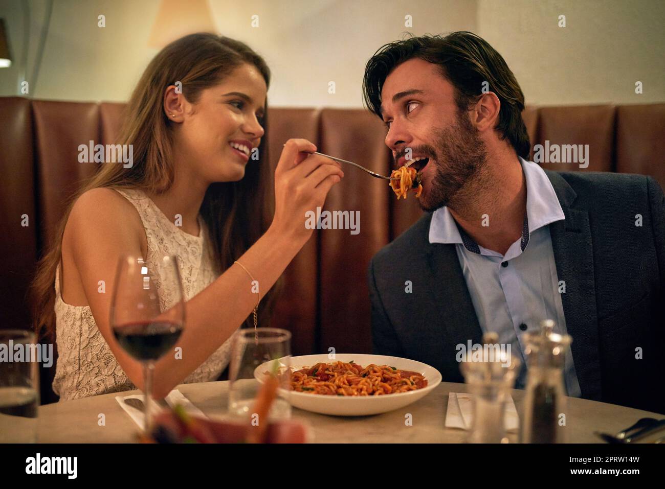 Amore al primo morso. una giovane donna che alimenta il suo ragazzo un forkful degli spaghetti durante una data romantica della cena ad un ristorante Foto Stock