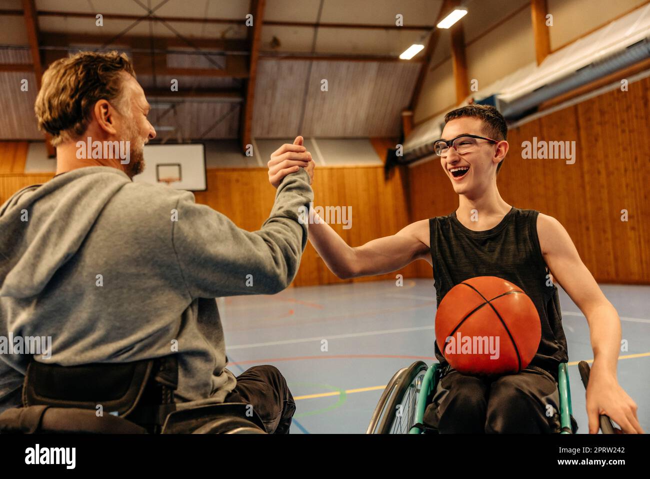 Allegri atleti di sesso maschile e femminile con disabilità che fanno stretta di mano mentre giocano a basket nel campo sportivo Foto Stock