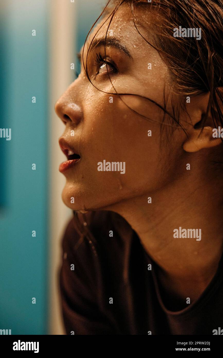 Atleta femminile con sudore sul viso che guarda lontano nello spogliatoio Foto Stock