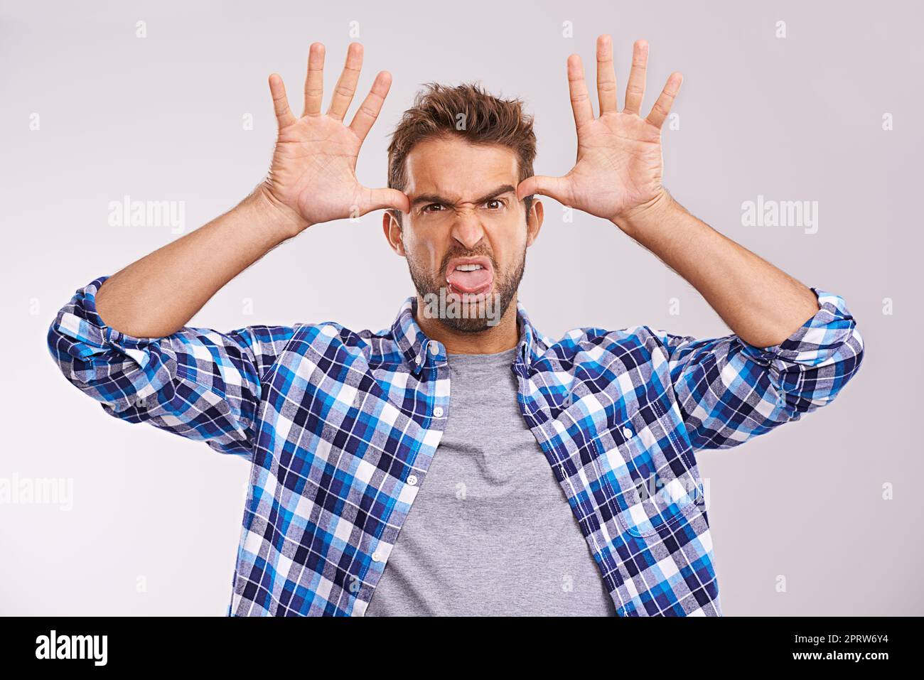 Aggiungi un po' di sciocco alla tua giornata. Un giovane che fa un volto su uno sfondo grigio. Foto Stock