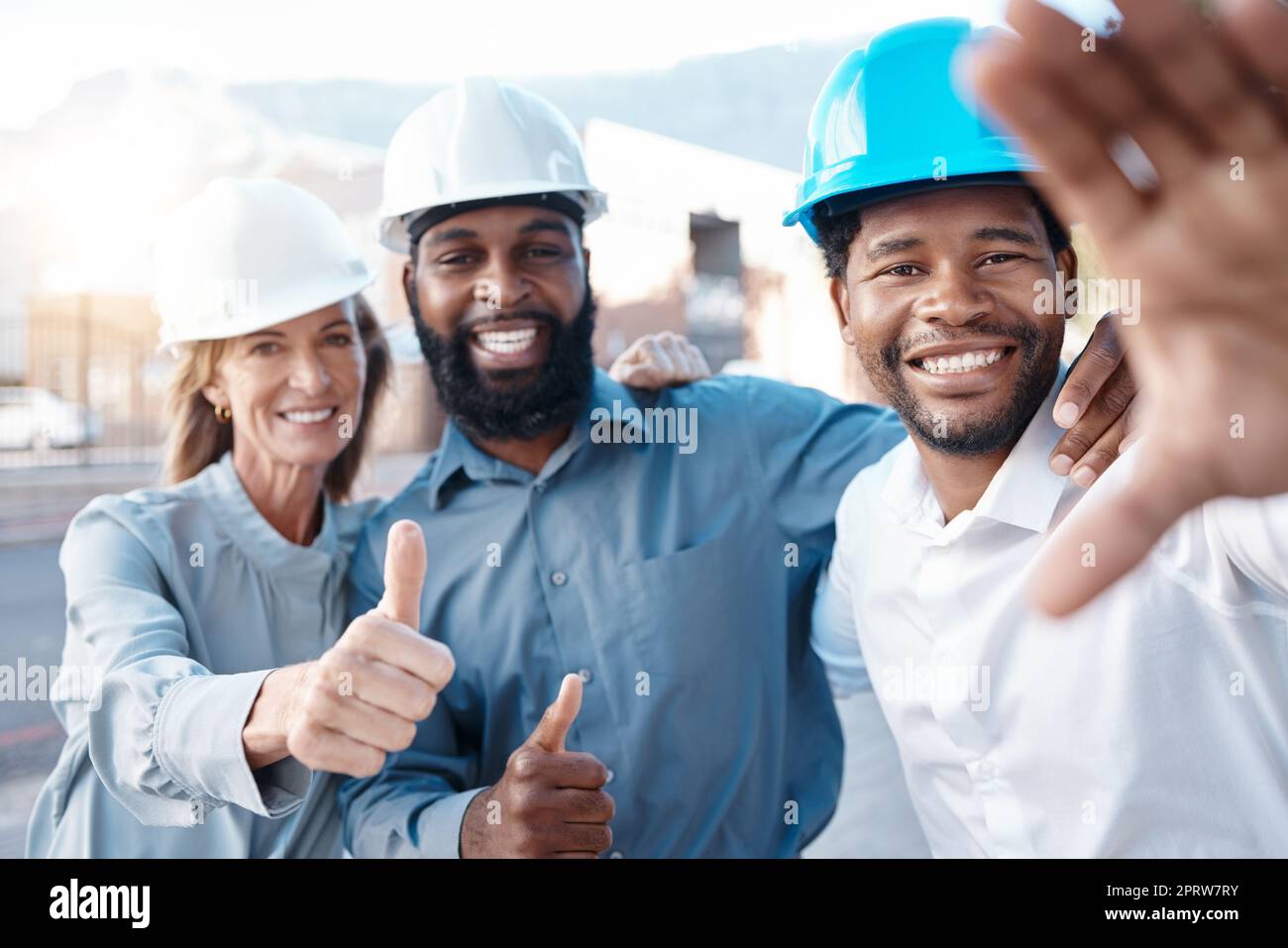 Selfie di cantiere e team soddisfatti con il pollice in alto durante la costruzione, la pianificazione e l'ingegneria. Architettura, sorriso e gruppo di architetti approvano la sicurezza di un progetto di sviluppo Foto Stock