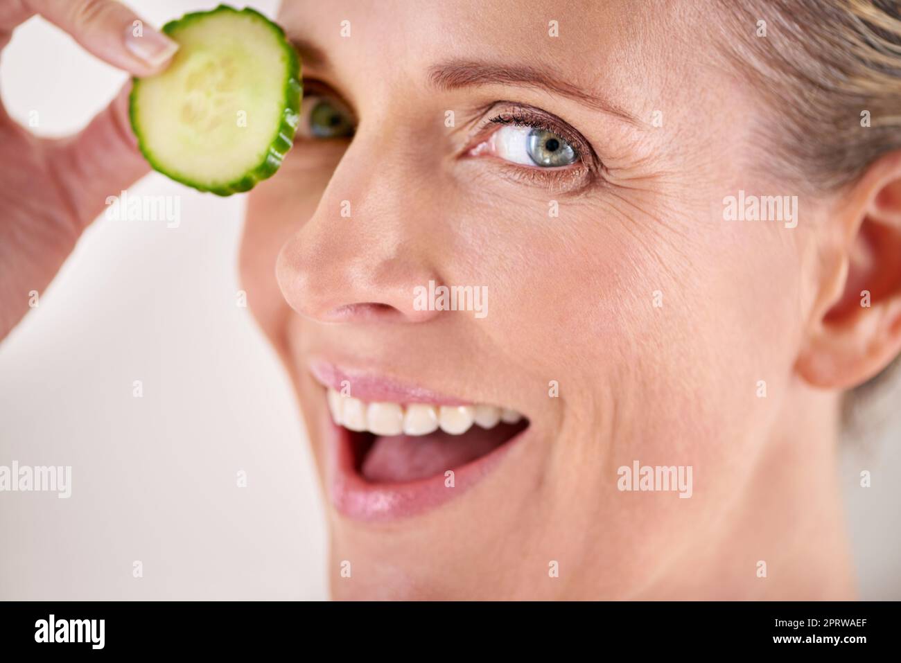 Rinfrescare la pelle con un po' di cetriolo. Ritratto corto studio di una donna matura che tiene una fetta di cetriolo ai suoi occhi. Foto Stock