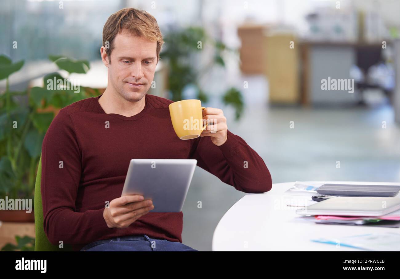 Prendendogli una pausa caffè con un po' di wifi. Un bel uomo d'affari che lavora alla sua scrivania. Foto Stock