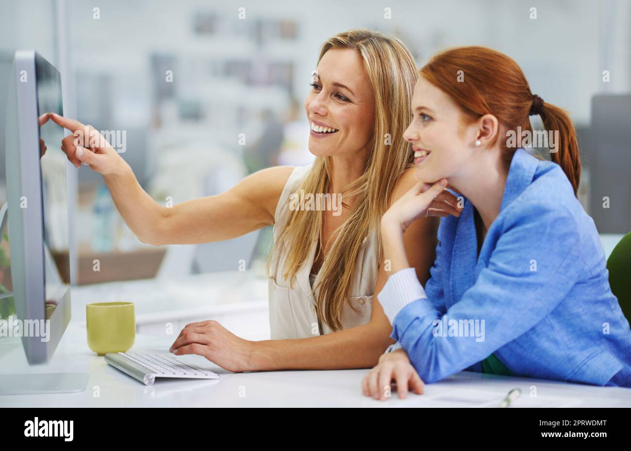 Guardate quanto può essere facile. Una collega attraente che mostra alla sua collega qualcosa di divertente sul suo computer. Foto Stock