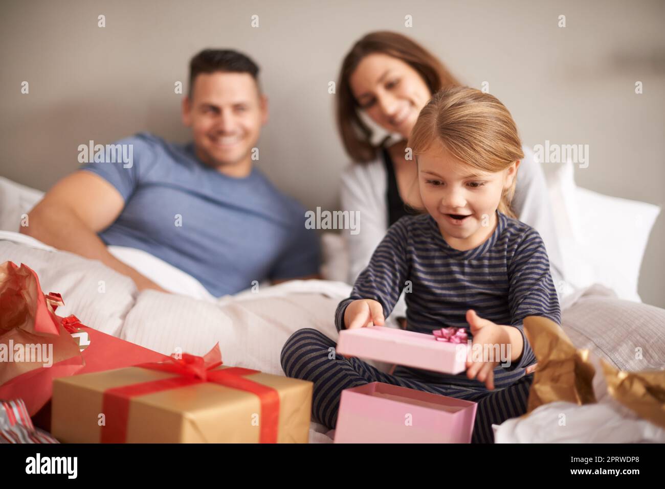 La grande apertura. Una bambina che riceve regali a letto dai suoi genitori. Foto Stock