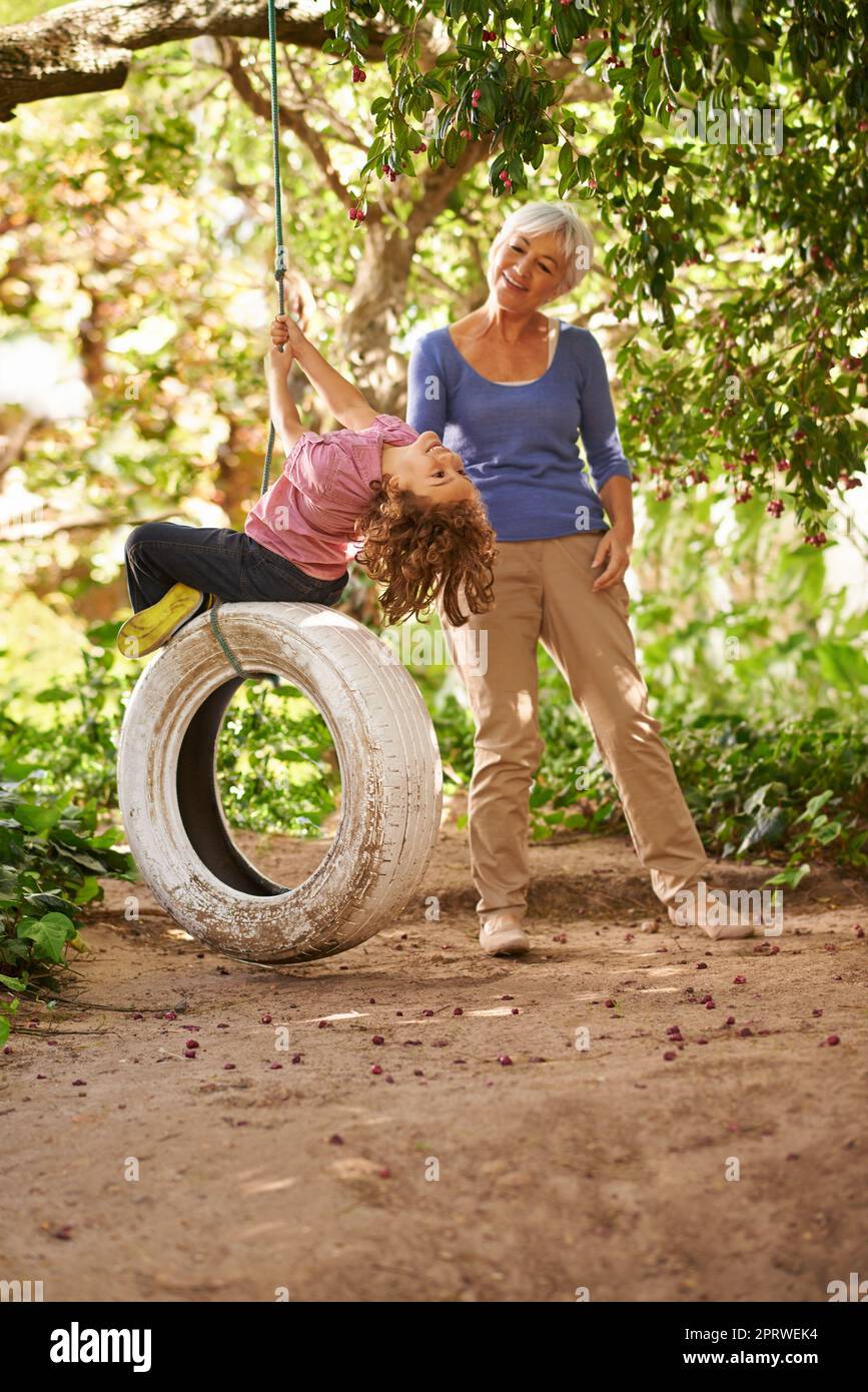 Godendo il avanti e indietro. Un giovane ragazzo che gioca su un'oscillazione di pneumatico mentre la sua nonna sta accanto. Foto Stock