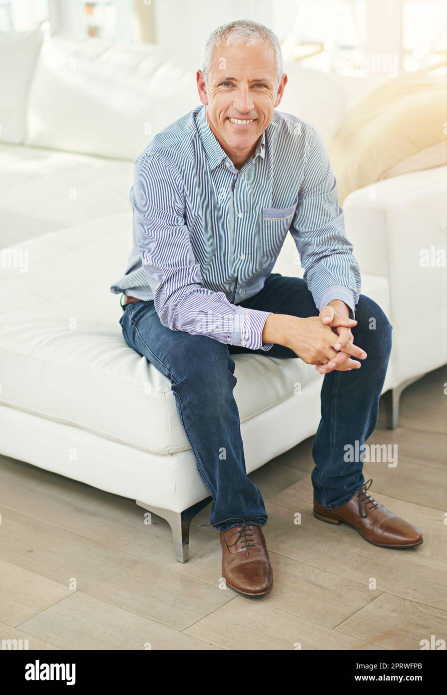 Felice a casa. Ritratto di un uomo maturo sorridente seduto su un divano nel suo salotto. Foto Stock