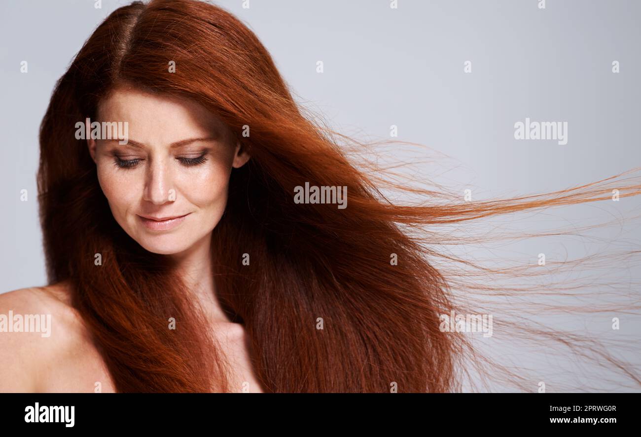 Capelli celesti. Studio shot di una giovane donna con bei capelli rossi che si posano su uno sfondo grigio. Foto Stock