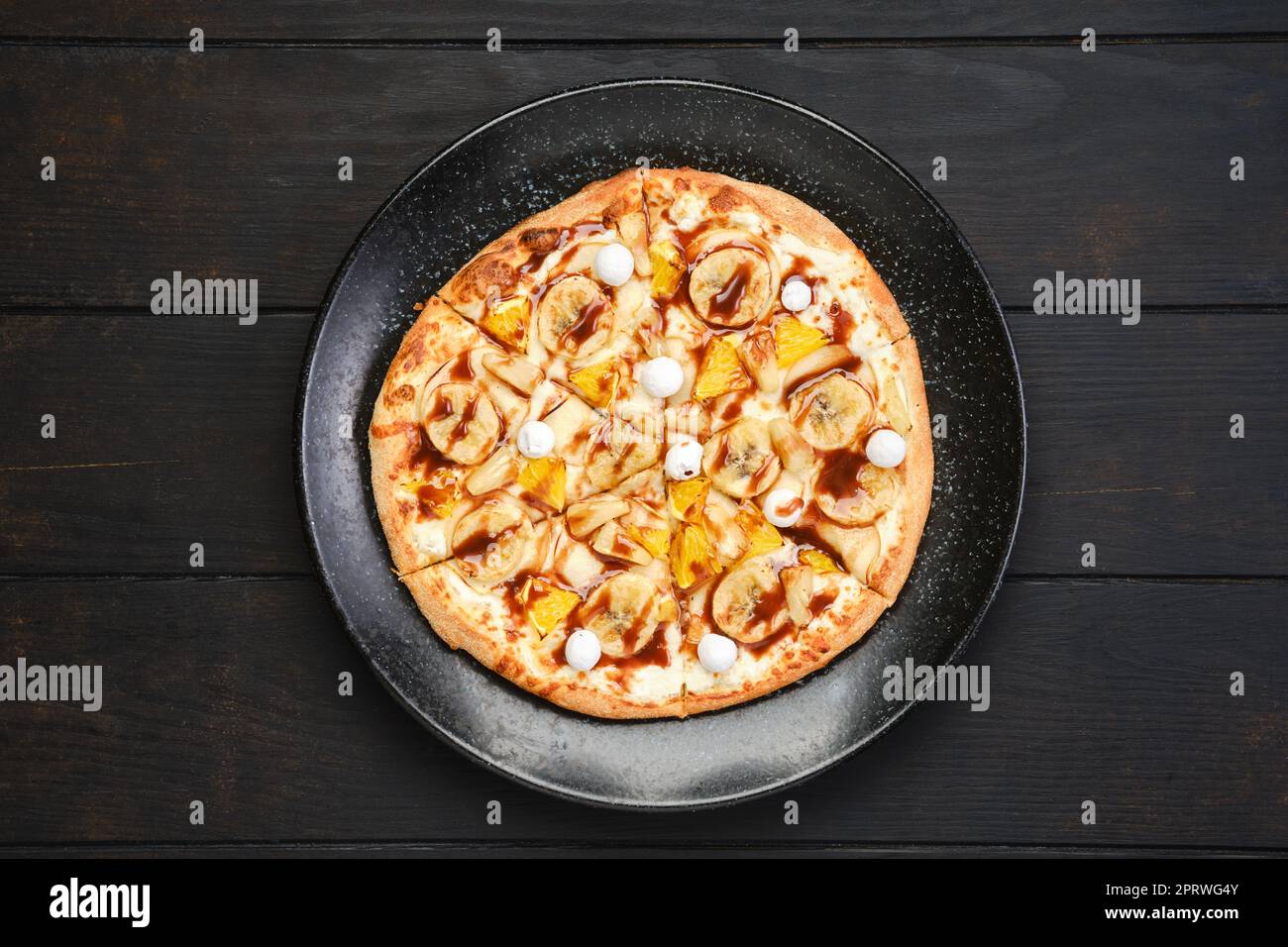 Vista dall'alto della torta dolce con banana, arancia, mirtilli rossi e sciroppo al caramello Foto Stock