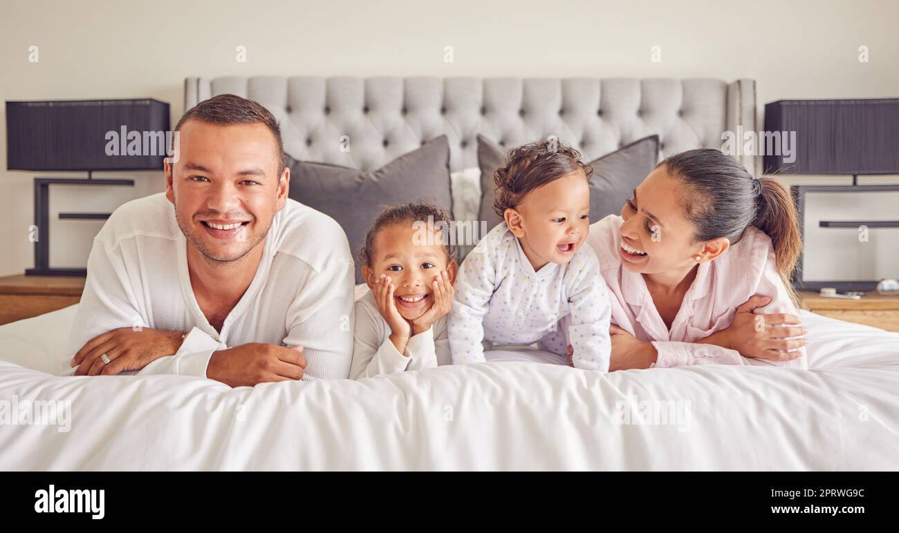 Ritratto della famiglia nella camera da letto di casa, i bambini sorridono sul letto e la madre ridendo con la felicità della bambina. Faccia di padre felice, coccole mattutine insieme e divertente mamma rilassati in pigiama durante il riposo del fine settimana Foto Stock