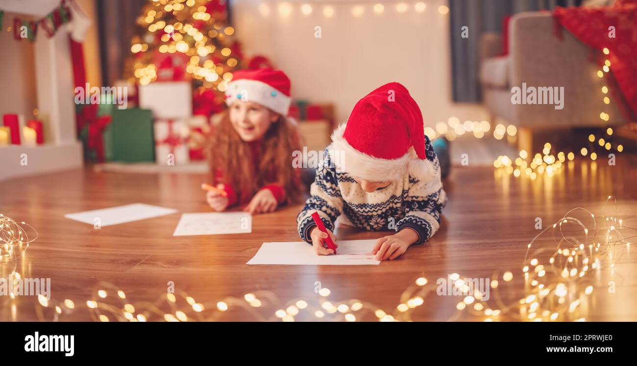 I bambini si trovano sul pavimento all'interno e scrivono lettere per Babbo Natale. Foto Stock