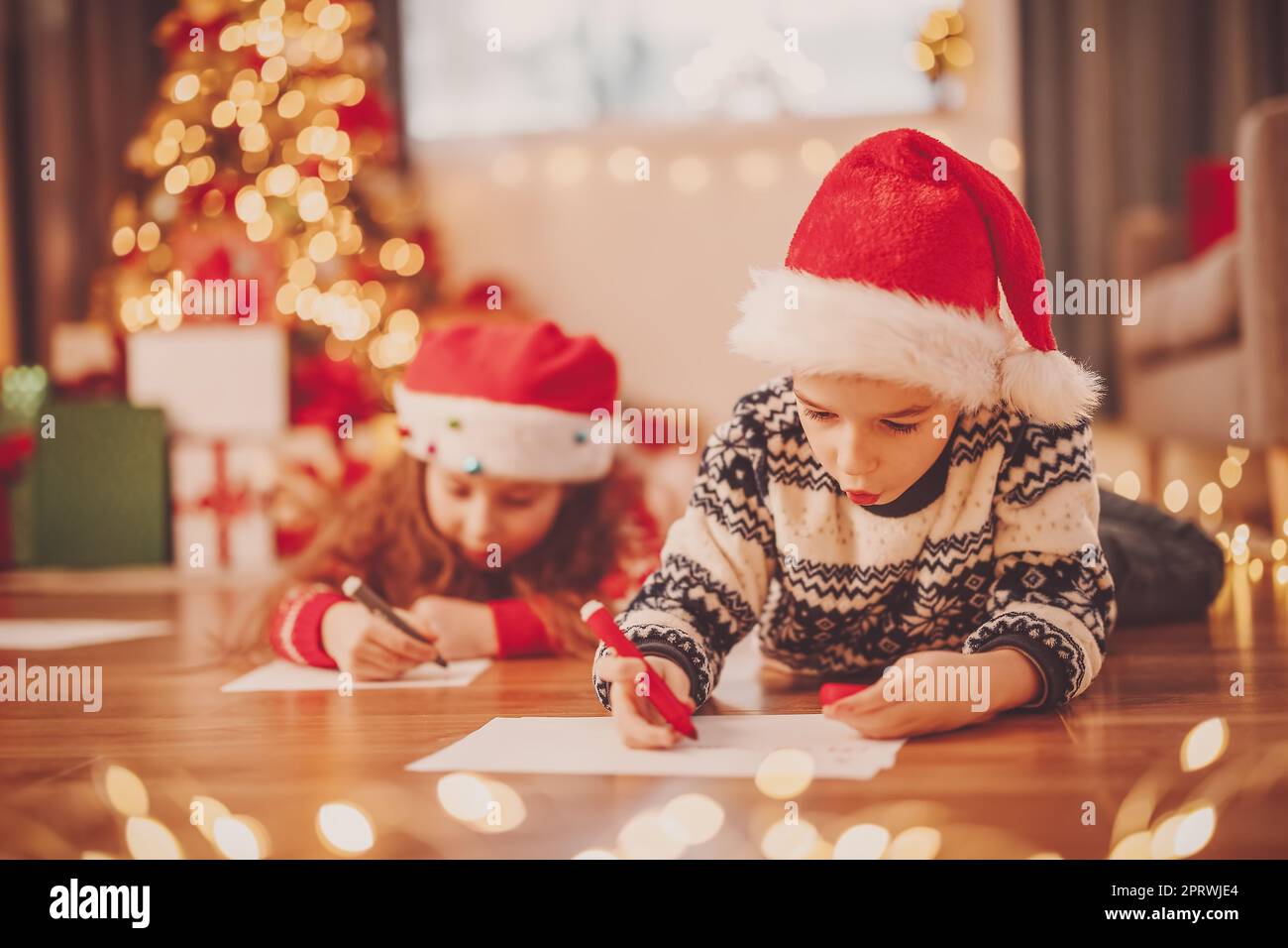 I bambini si trovano sul pavimento all'interno e scrivono lettere per Babbo Natale. Foto Stock