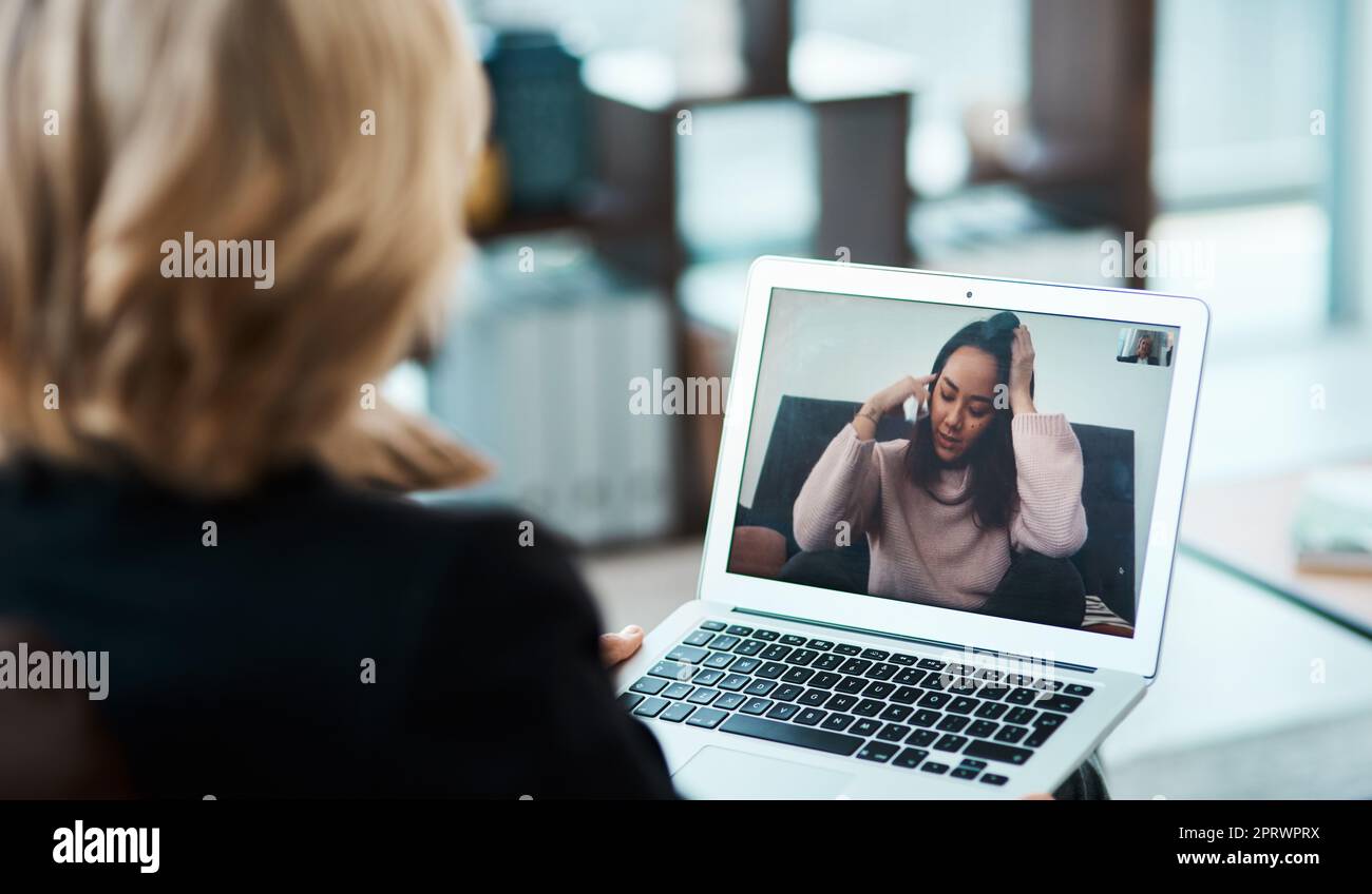 In tempi di incertezza, una giovane donna che ha una sessione di consulenza con uno psicologo utilizzando uno strumento di videoconferenza. Foto Stock