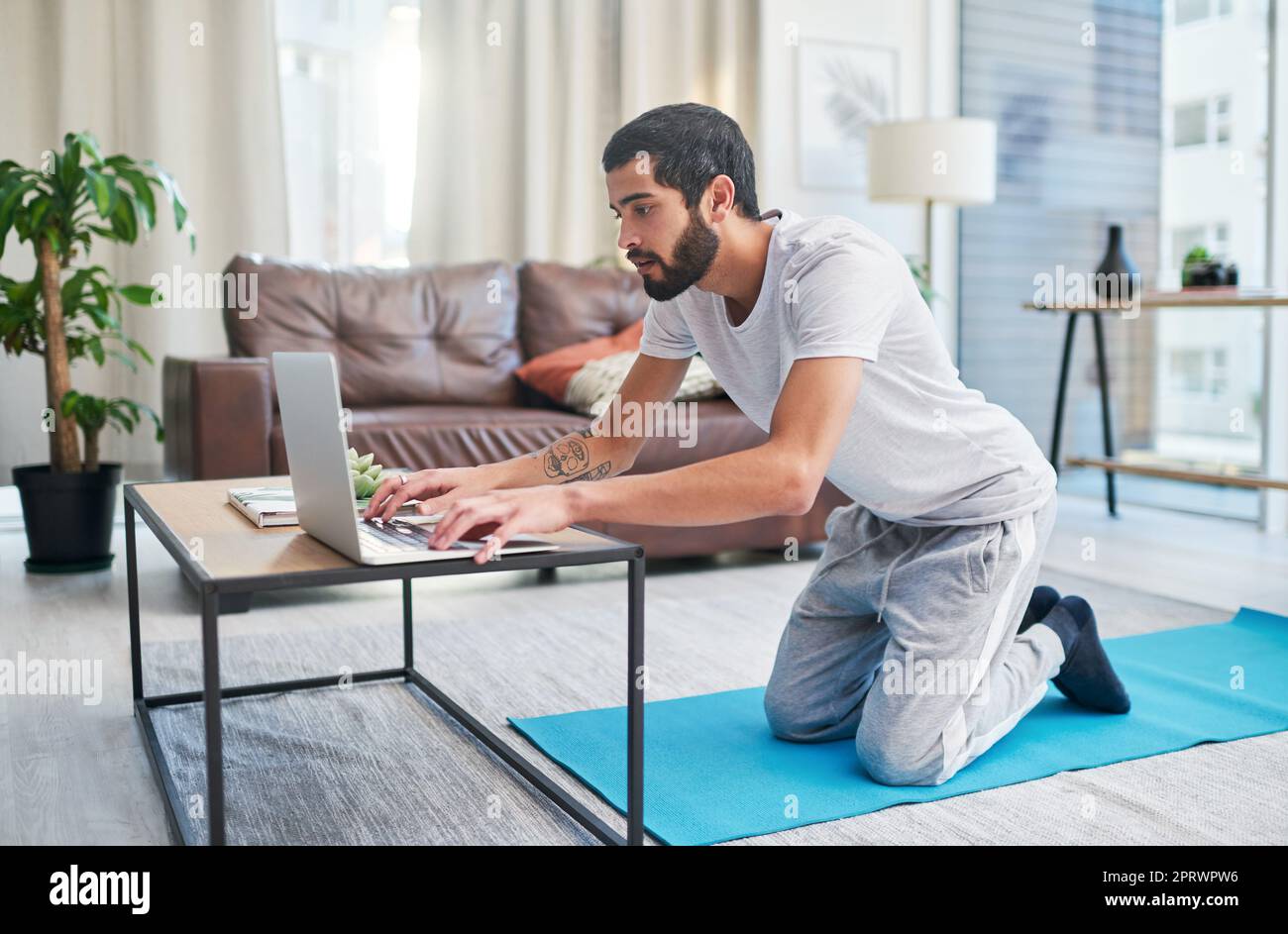 Ho alcuni video per replicare gli allenamenti in palestra a casa. Un uomo che usa il suo laptop mentre pratica lo yoga a casa. Foto Stock