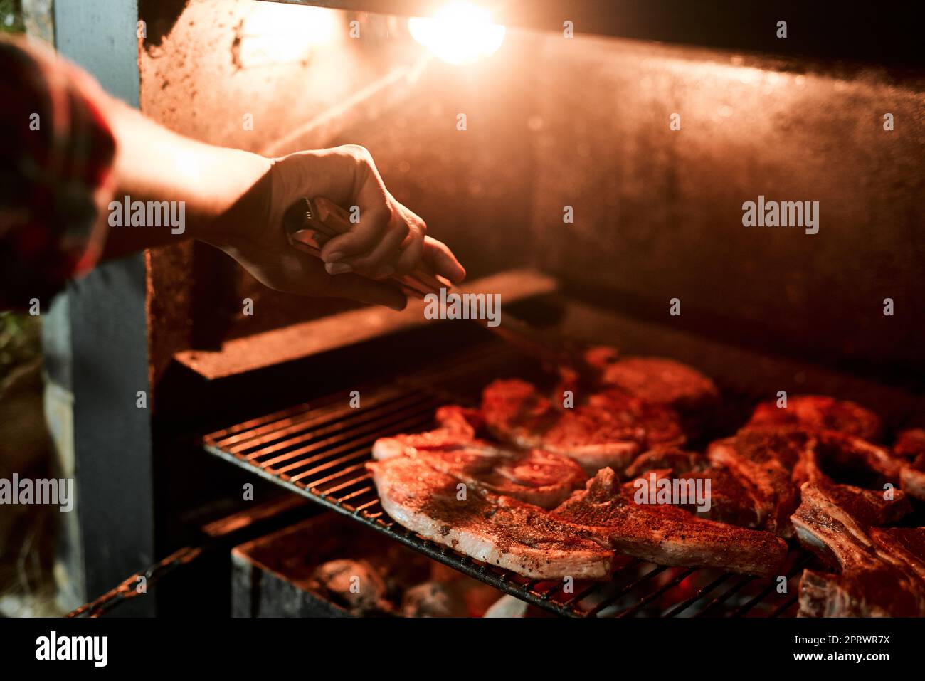 Il gusto del cibo alla griglia è così unico. Primo piano di un uomo irriconoscibile grigliare carne mentre si fa un barbecue. Foto Stock