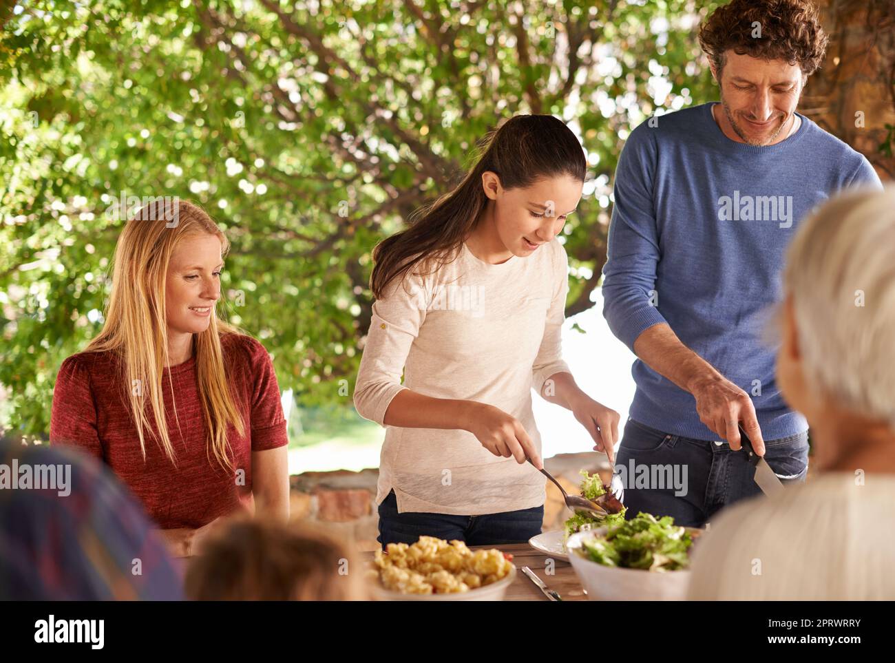 Aiutare papà piatto su. Una vista di una famiglia che si prepara a pranzare insieme all'aperto. Foto Stock
