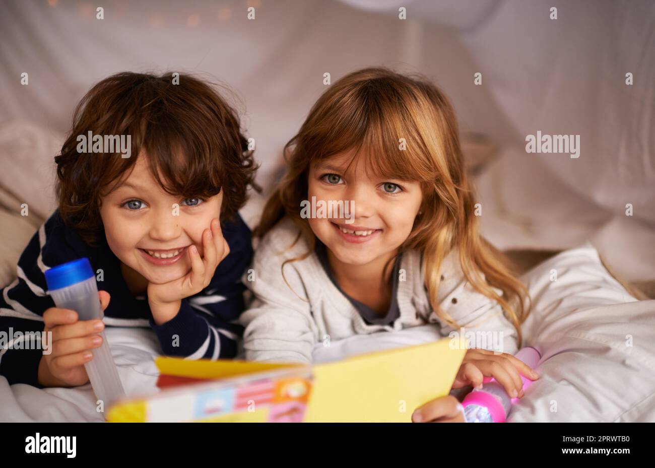 Vivete, amate e imparate insieme. Due adorabili fratelli che usano le torce per leggere un libro all'interno della loro fortezza coperta. Foto Stock