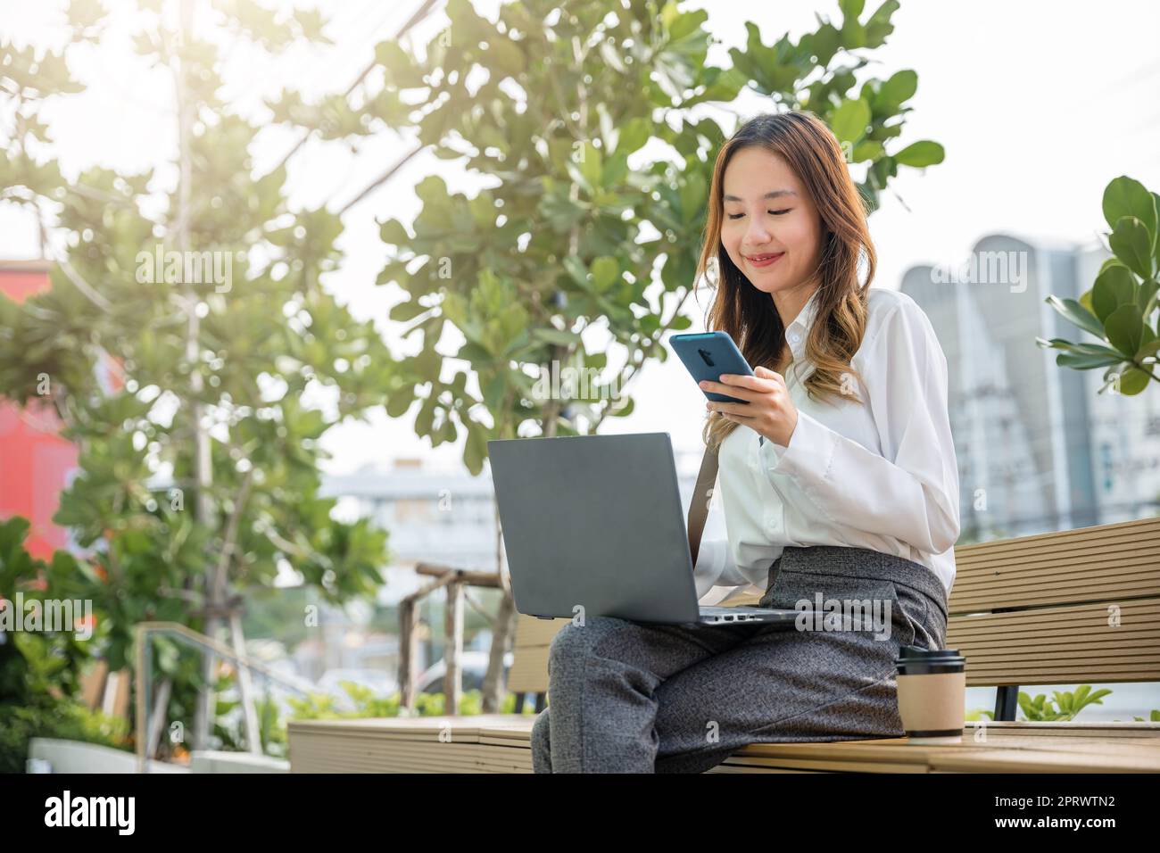 giovane donna che lavora con un computer portatile e utilizza uno smartphone mobile all'esterno dell'edificio Foto Stock