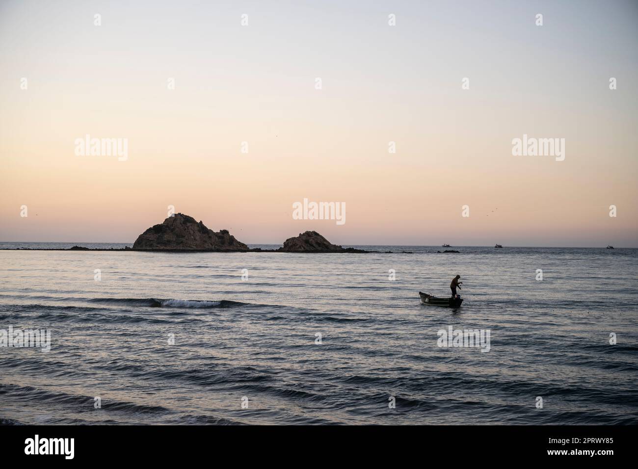Silhouette di un pescatore che si prepara a gettare le reti in mare al tramonto. Foto Stock