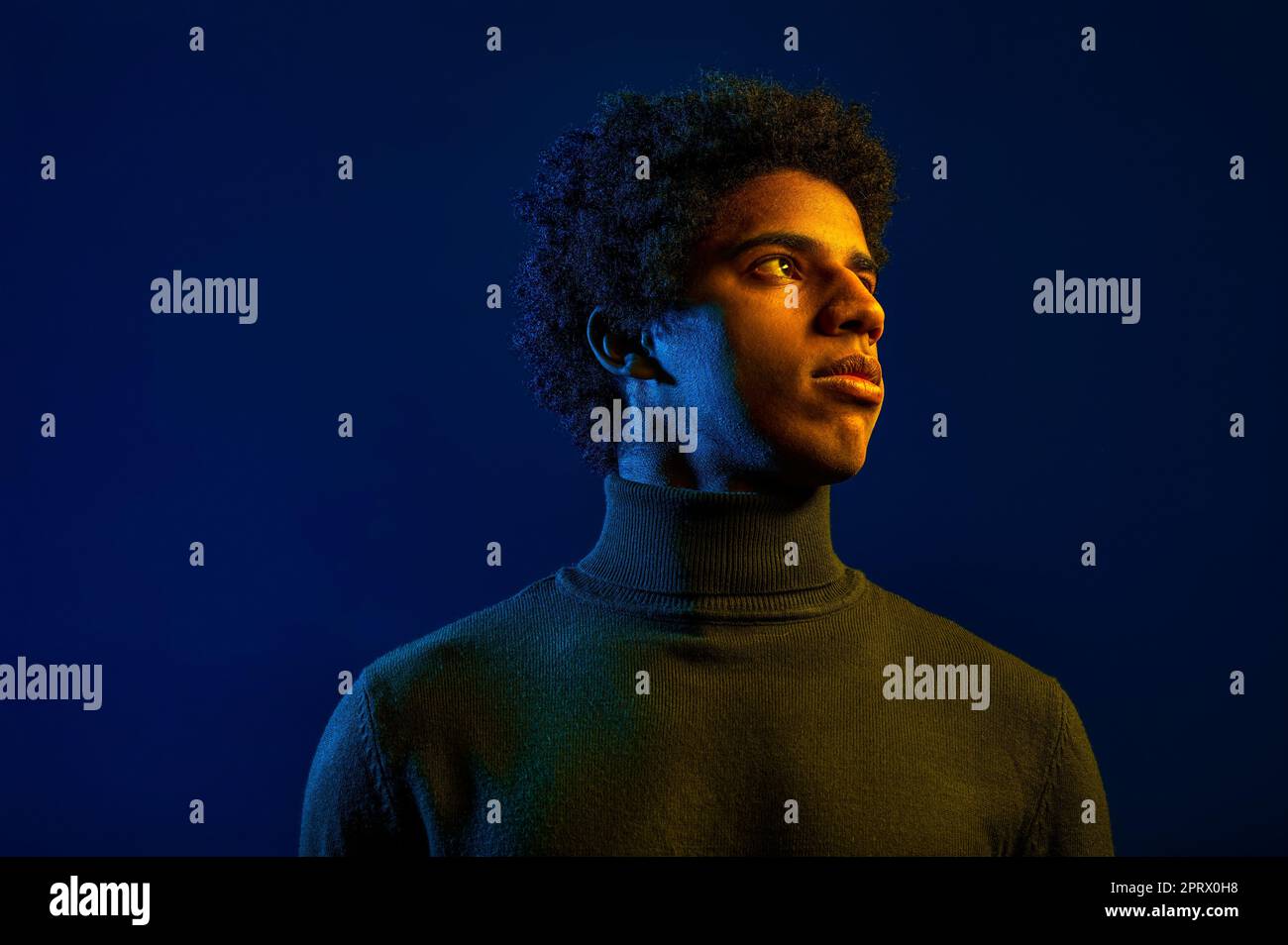 Giovane uomo serio che guarda via sullo sfondo scuro dello studio Foto Stock