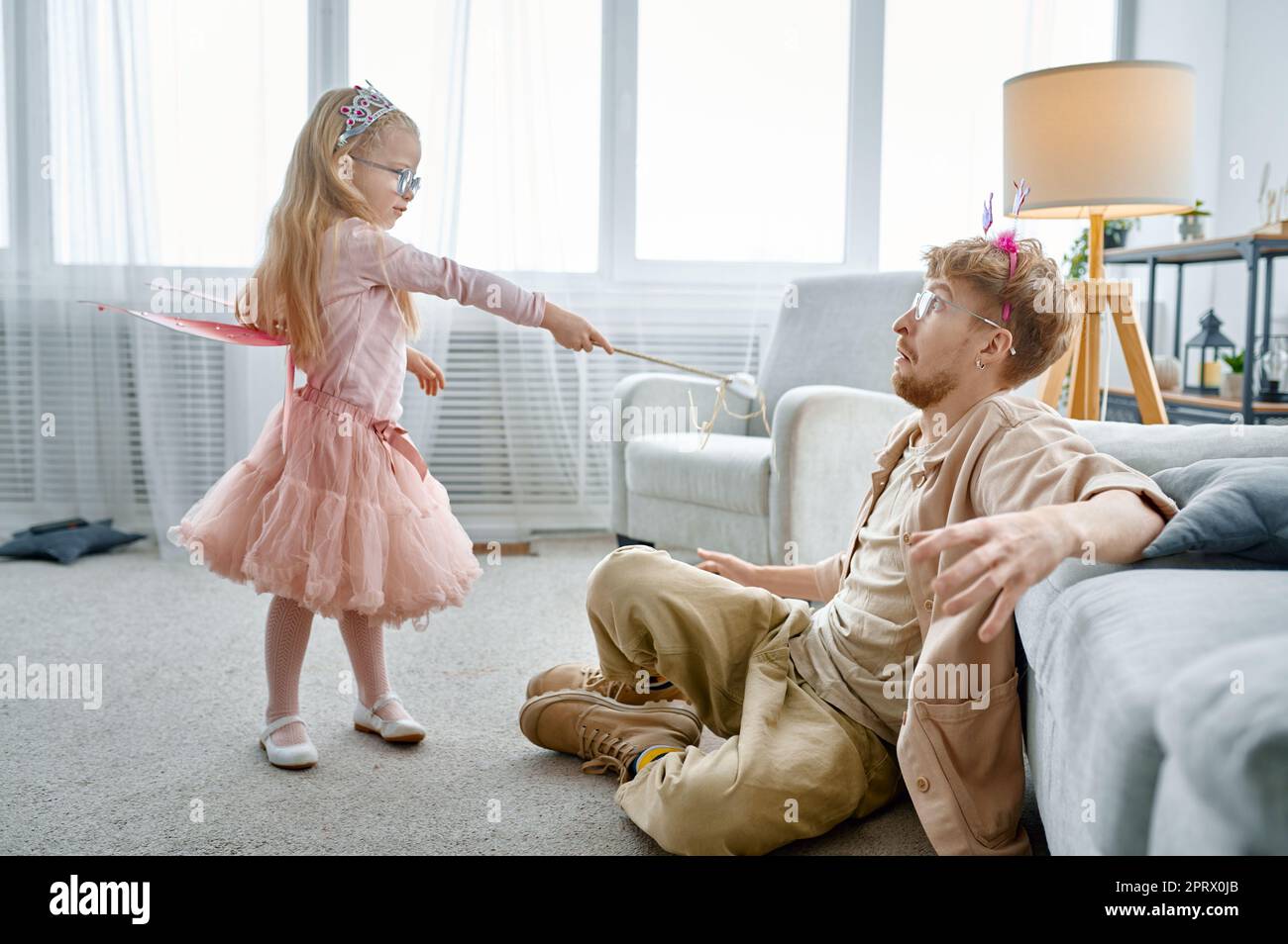 Piccola figlia carina con bacchetta magica e padre che scherzano a casa Foto Stock