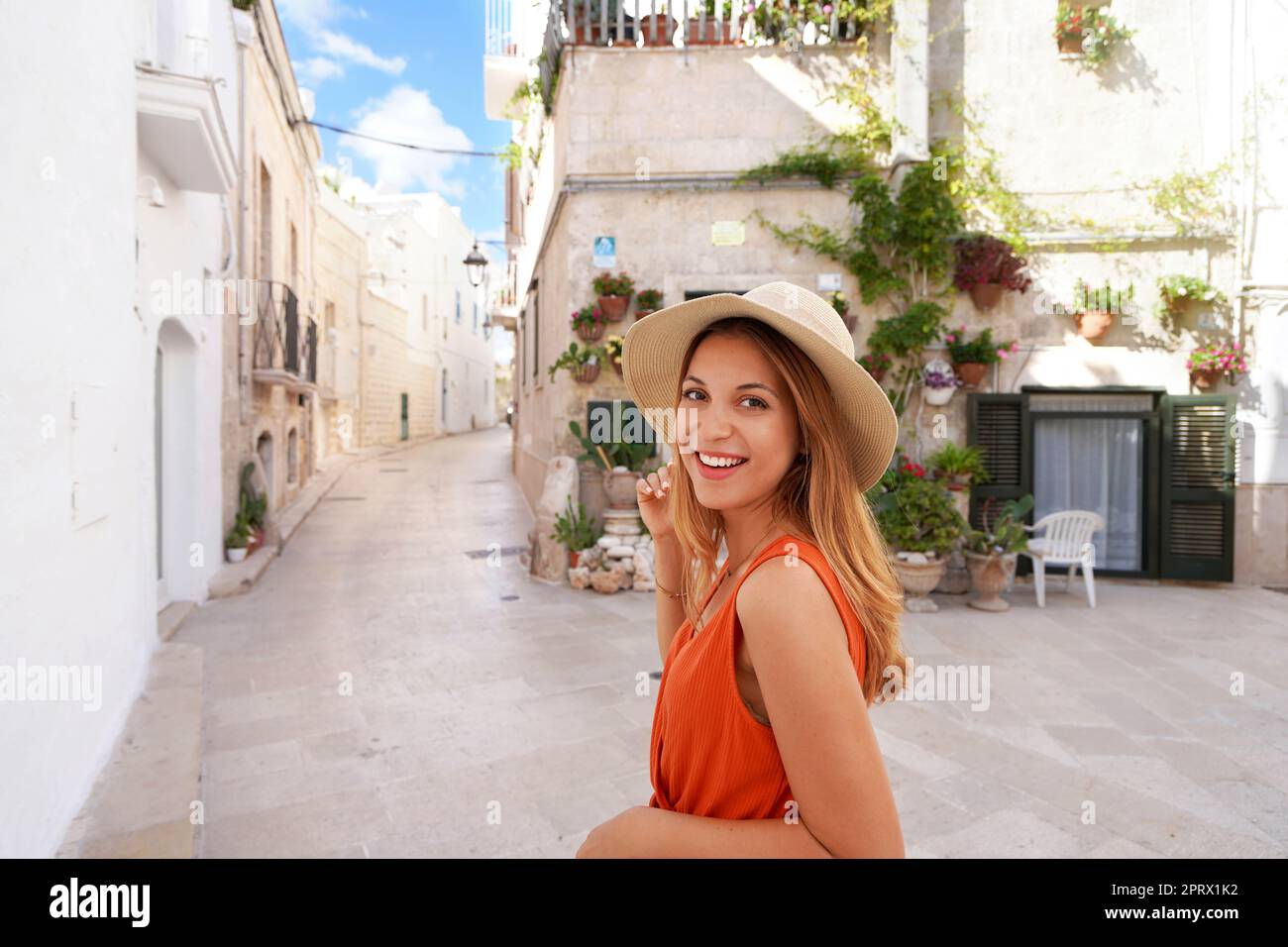 Bella giovane donna gioiosa che sorride e guarda la macchina fotografica. Ritratto di una giovane donna abbronzata con cappello e abito arancione che si gode le vacanze estive in Italia. Foto Stock