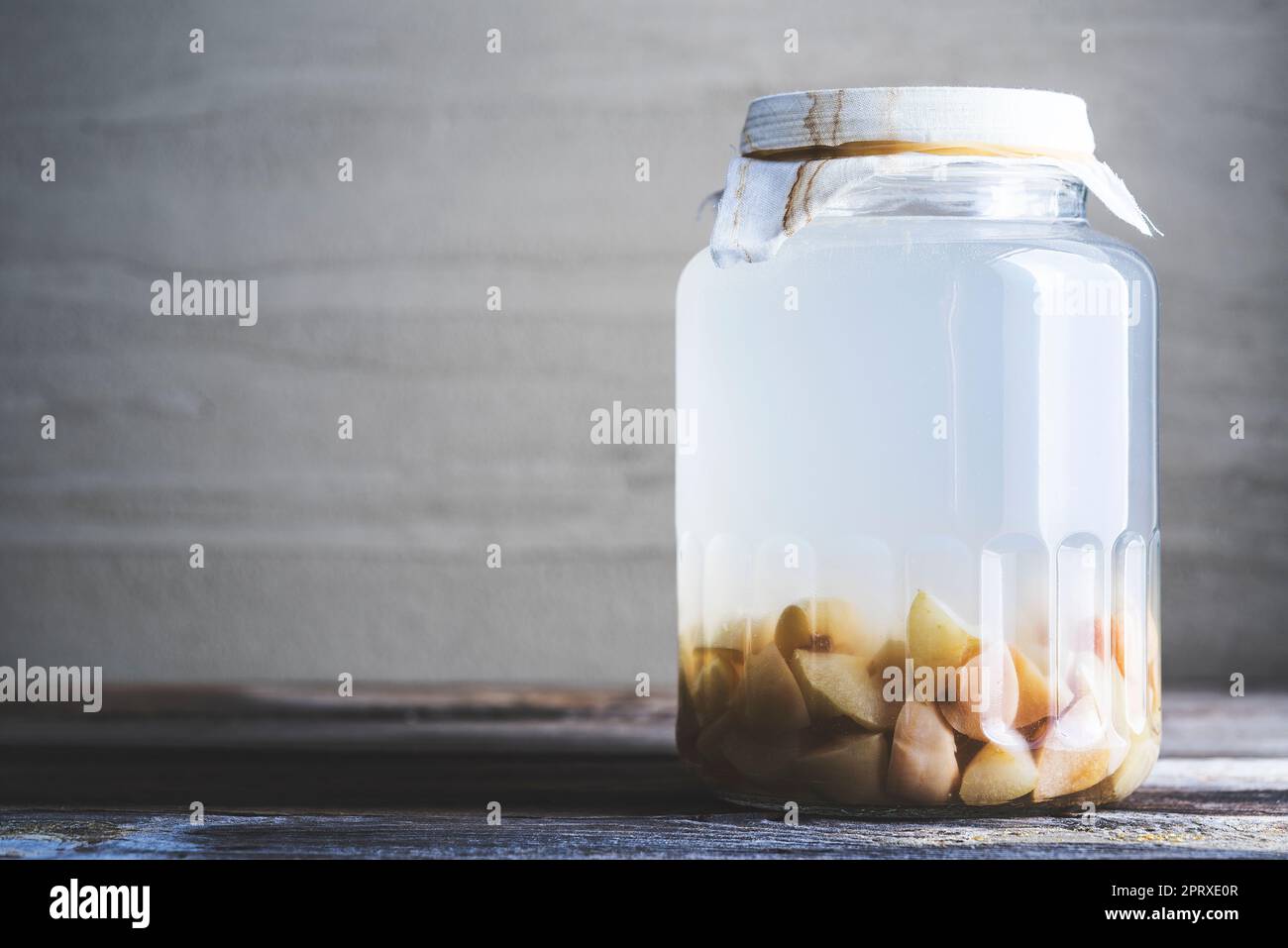 Bottiglia di aceto di sidro di mela su fondo rustico, vaso coperto di cheesecloth . Foto Stock